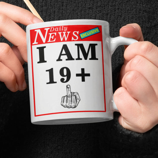 Mug with 'I AM 19+1 middle finge' text and newspaper design held by hands against a dark background