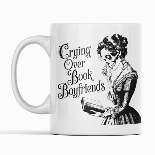 White mug. Lady skeleton reading a book. Text Crying over book boyfriends. 