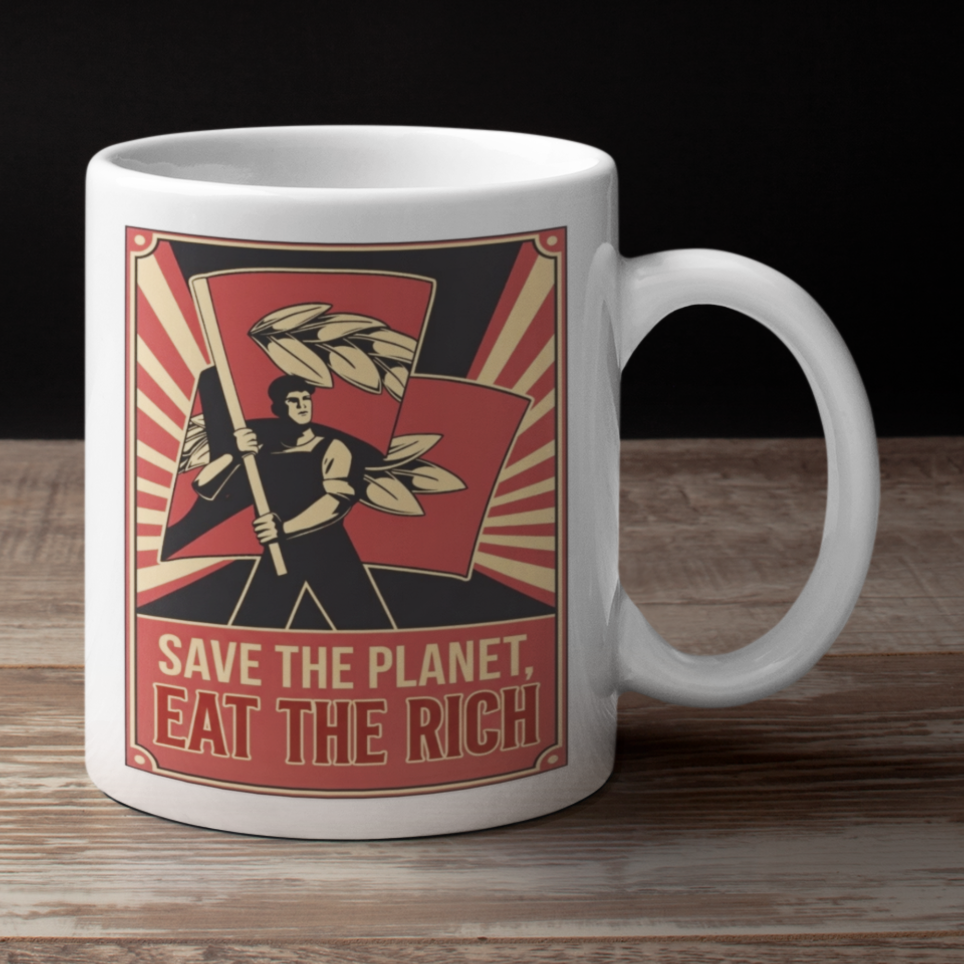 White mug with a graphic design featuring a person holding a staff  and text 'Save the Planet, Eat the Rich' on a wooden surface.